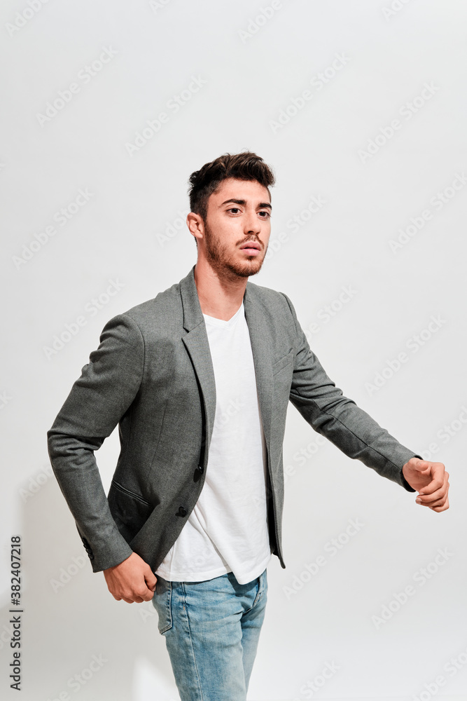 Young man wearing jeans, a white tshit iand a grey blazer walking in front of a white wall. Young man wearing jeans, a white tshit iand a grey blazer walking in front of a white wall.