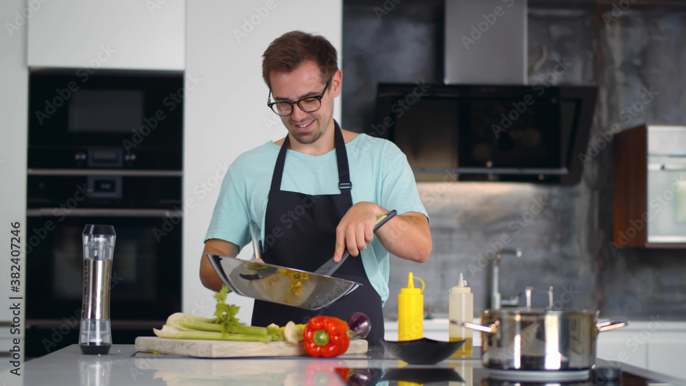 Portrait of focused young man chef cook tasty dish in pan at modern kitchen Portrait of focused young man chef cook tasty dish in pan at modern kitchen