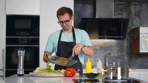 Fototapeta Naklejka Na Ścianę i Meble -  Portrait of focused young man chef cook tasty dish in pan at modern kitchen
