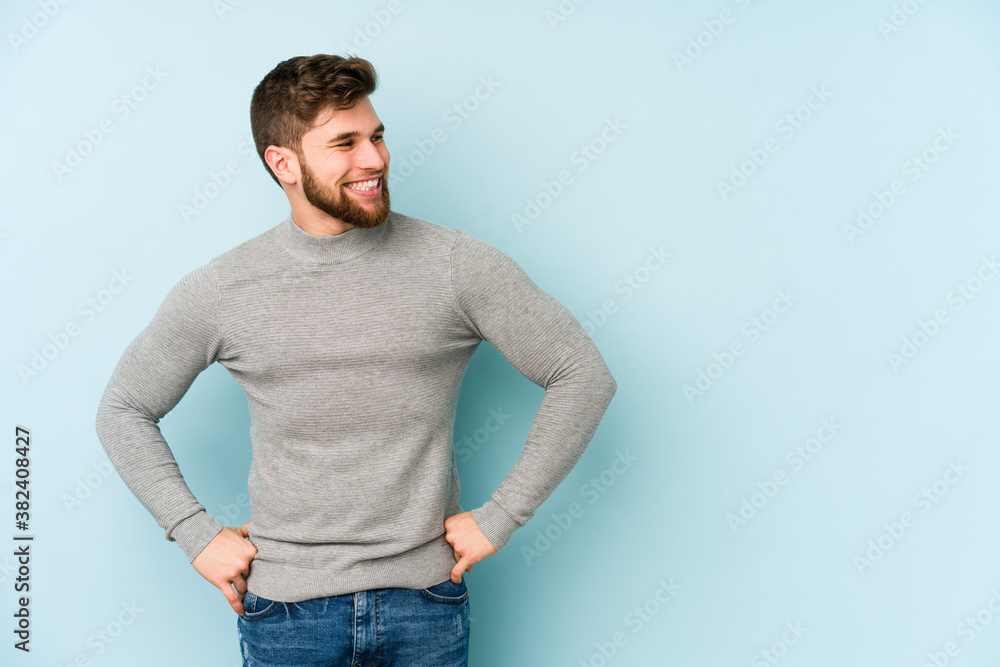 Young caucasian man isolated on blue background laughs happily and has fun keeping hands on stomach. Young caucasian man isolated on blue background laughs happily and has fun keeping hands on stomach.