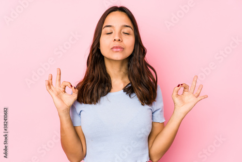 Young mixed race hispanic woman isolated relaxes after hard working day, she is performing yoga.