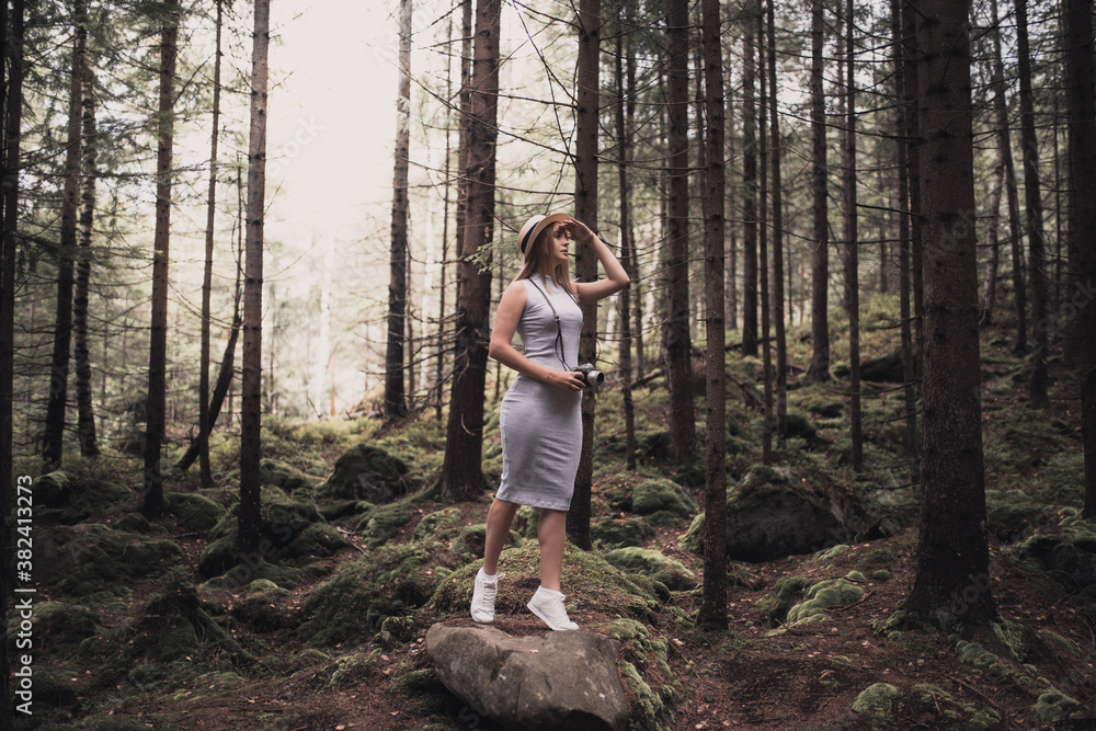 Slavic tanned fair-haired young girl with a boater hat on nature. Traveler tourist in a dark forest. constant tone of clothes. dark brown background Slavic tanned fair-haired young girl with a boater hat on nature. Traveler tourist in a dark forest. constant tone of clothes. dark brown background