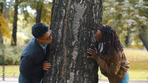 Young multiethnic couple in love hugging tree trunk in autumn park