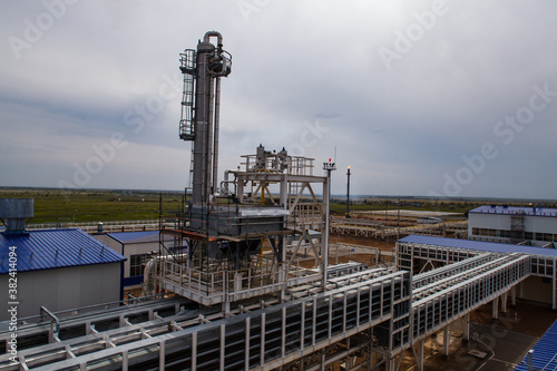 Oil refinery plant on grey sky background. Distillation tower and pipelines and burning gas torch.