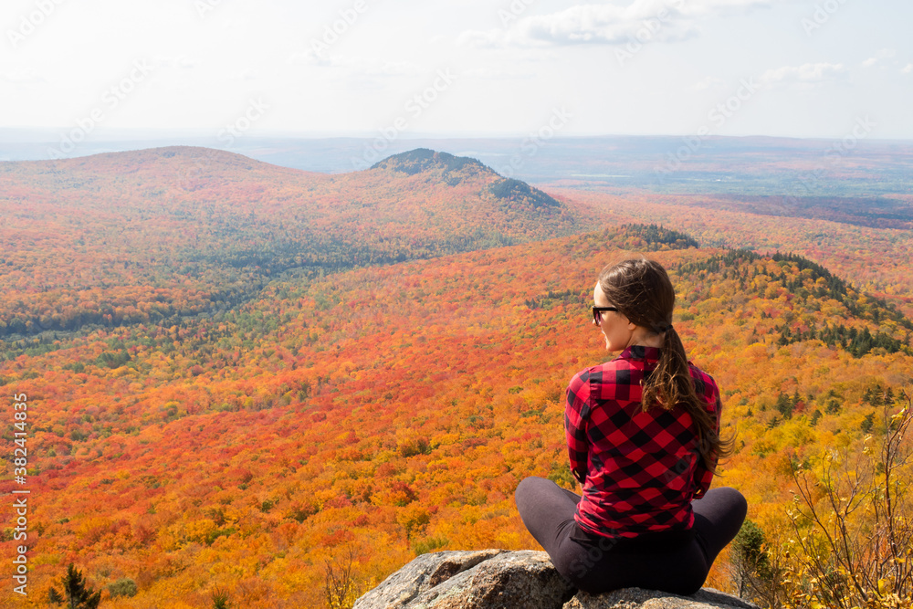 Back view of a young woman sitting in the Mégantic national park and admiring the autumnal colors, Canada