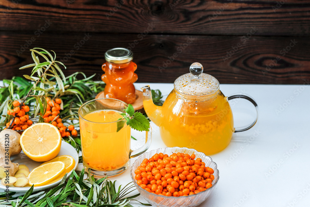 Sea buckthorn tea with lemon, ginger and honey on a white table on a wooden background Sea buckthorn tea with lemon, ginger and honey on a white table on a wooden background
