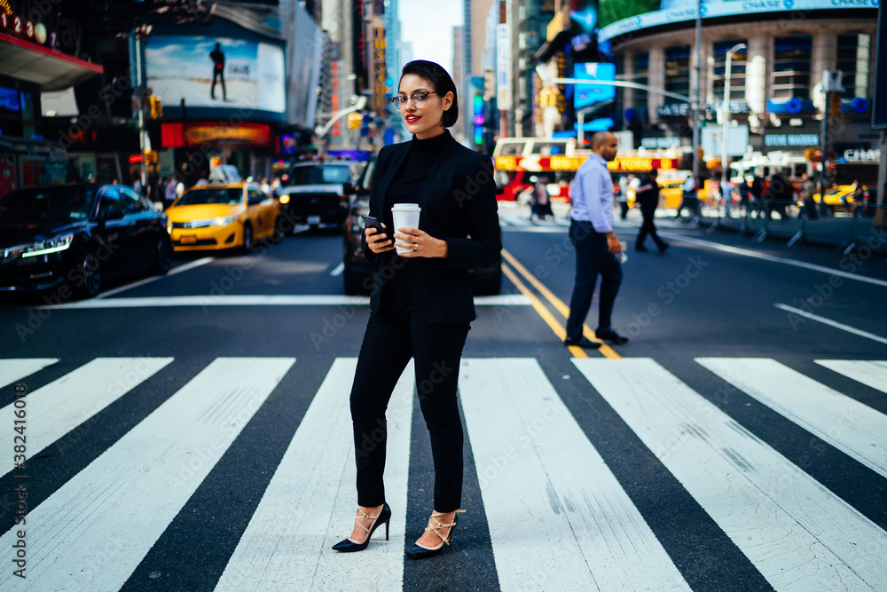 Cheerful lady with coffee and cellphone on crosswalk