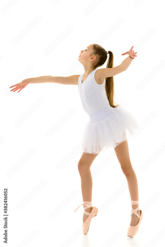 Cute little girl in a tutu and pointe shoes dancing in the studio on a white background.