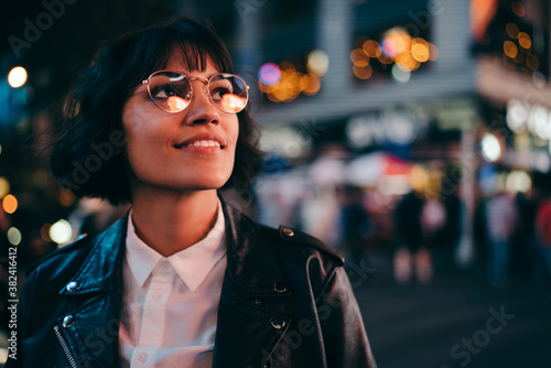 Carefree brunette young woman with short haircut in stylish eyewear for eyes protection fascinated with New York urbanity in Manhattan,youthful female in leather jacket enjoying metropolitan nightlife