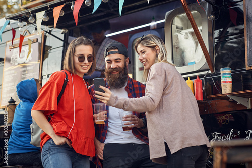 Group of friends drinking beer in front of food truck; Urban lifestyle concept