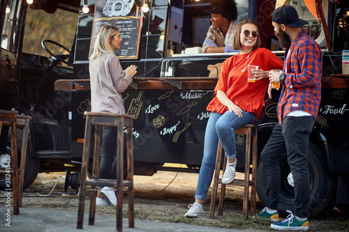 Friends drinking beer in front of food truck; Urban lifestyle concept