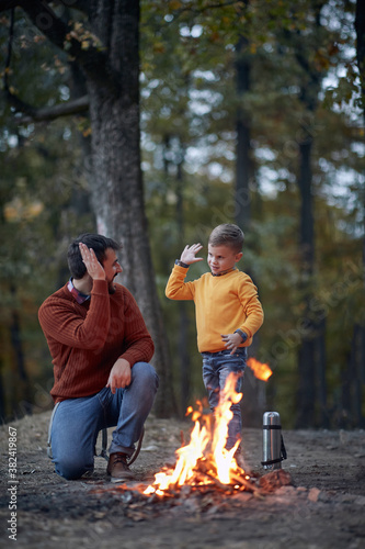 Fototapeta Dad and son starting a fire; Spring or autumn camping with campfire at night ; camping, travel, tourism, hike and people concept