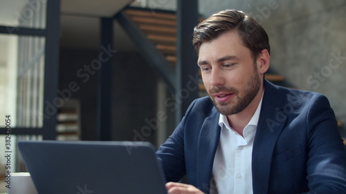 Smiling businessman working with laptop computer and papers in office.