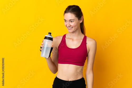 Young Ireland woman isolated on yellow background with sports water bottle