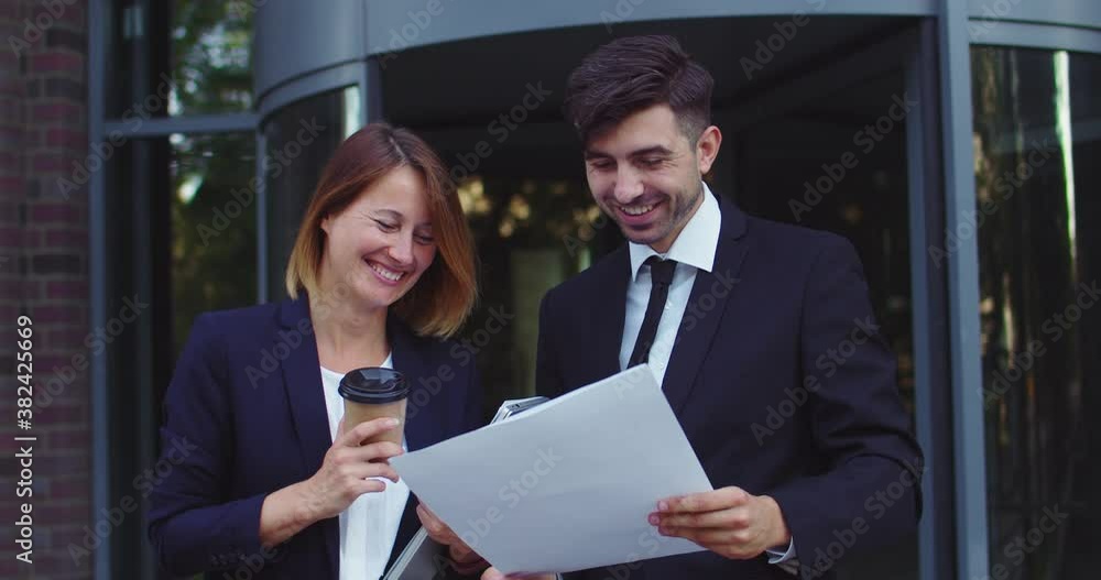 Good-looking business partners talking suring coffee break time outdoors. Caucasian man and woman collegues discussing project outside company building. Work, profession, occupation concept. Good-looking business partners talking suring coffee break time outdoors. Caucasian man and woman collegues discussing project outside company building. Work, profession, occupation concept.
