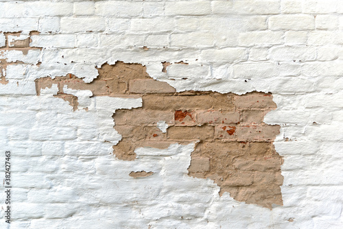 Textured surface of abandoned building wall made of weathered brown bricks covered with flaked white color stucco at bright sunlight extreme close view