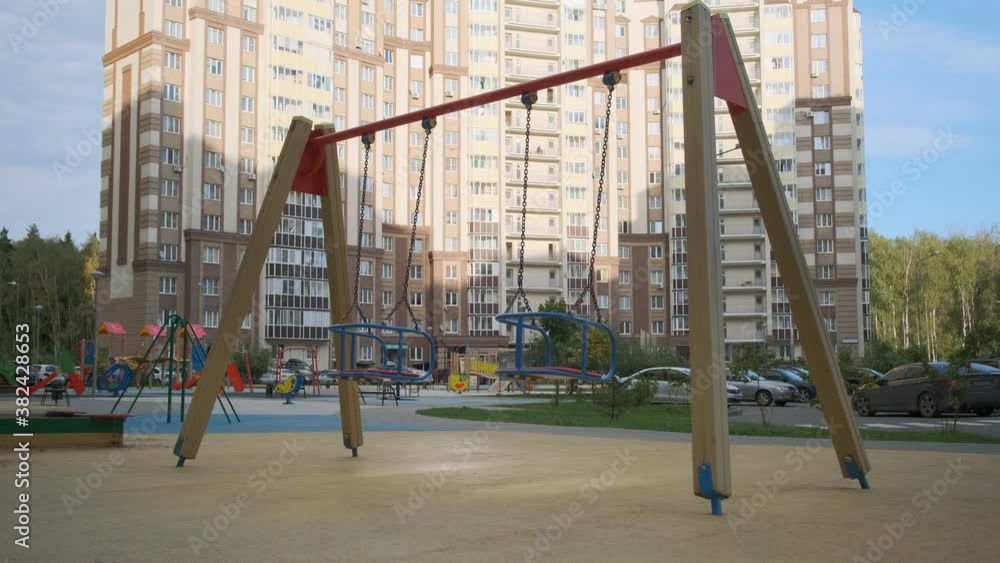 Empty swing on children playground against background of multi-storey residential building in big city. Empty swing on children playground against background of multi-storey residential building in big city.