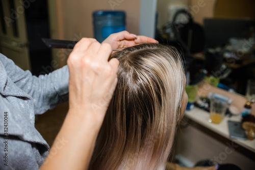Master hairdresser combs the hair of a young woman, blonde. Haircut. Home beauty salon. 