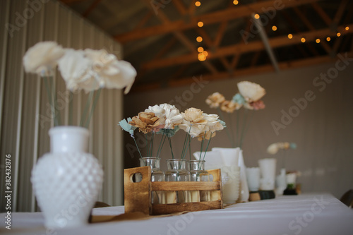 Balsa wood biodegradable wedding flower centerpieces in milk glass and small vases. Rustic wedding centerpieces in a barn with string lights