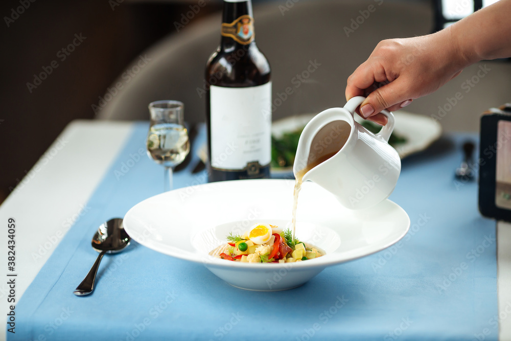 Pouring broth in a plate with soup vegetables