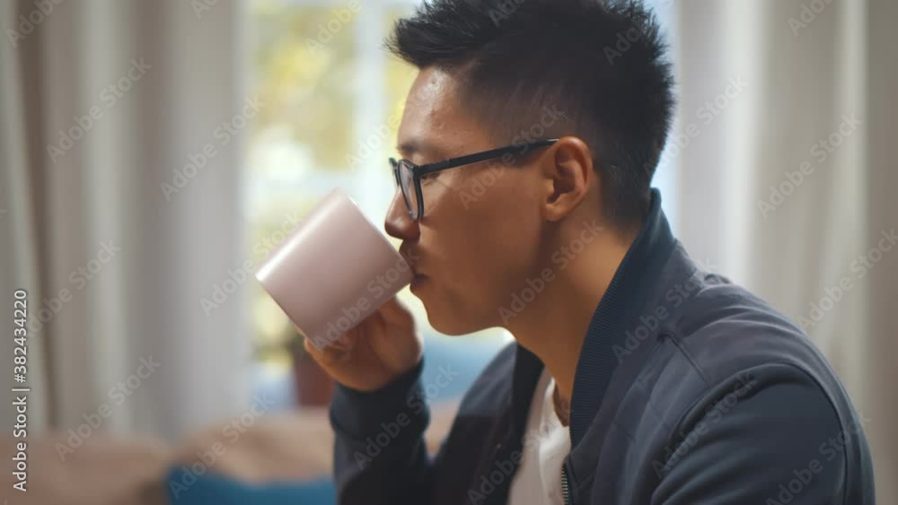 Close up of young asian man working on laptop drinking coffee at home office Close up of young asian man working on laptop drinking coffee at home office