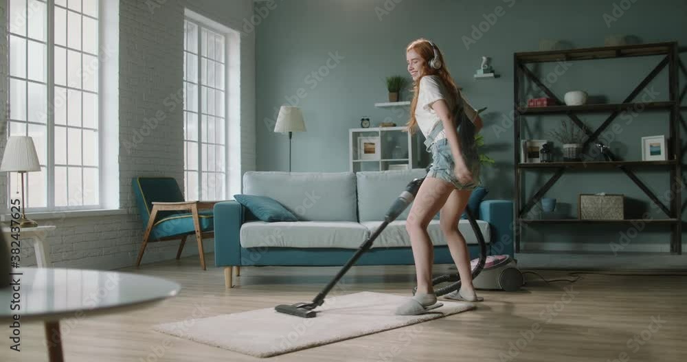Cute caucasian girl cleaning her house with joy. Positive happy woman using a vacuum cleaner, listening to music in headphones and dancing - happy people 4k footage Cute caucasian girl cleaning her house with joy. Positive happy woman using a vacuum cleaner, listening to music in headphones and dancing - happy people 4k footage
