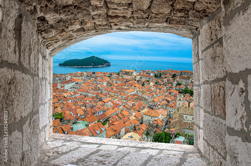 View from stone window of red rooftops in Dubrovnik old tow. Beautiful view of blue sea, island and old historical center in Dubrovnik, Croatia