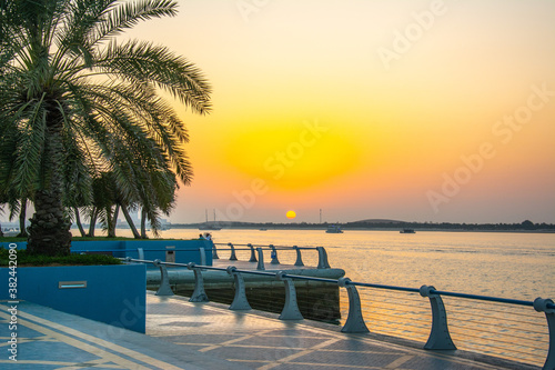 The view of the Persian Gulf, Corniche promenade with palm trees on sunset in Abu Dhabi, United Arab Emirates