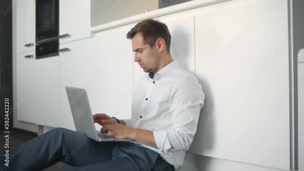 Young caucasian businessman working from home sitting on kitchen floor using laptop Young caucasian businessman working from home sitting on kitchen floor using laptop
