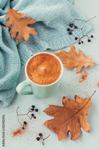 Blue cup of coffee with autumnal dry leaves and dry berries on a light background. Autumn mood concept.