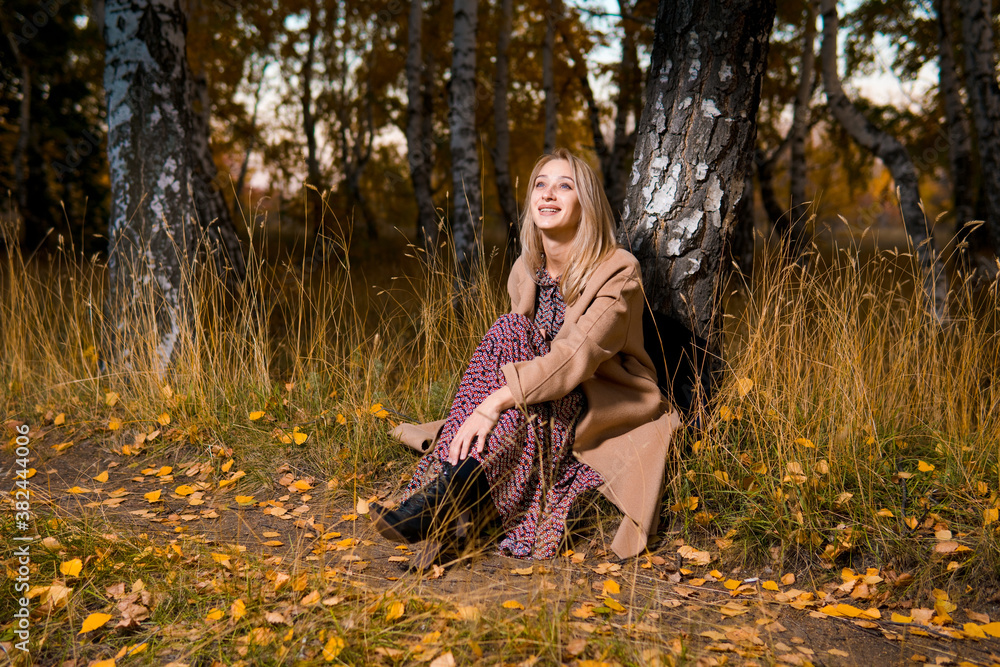 Young beautiful smiling woman in long coat sitting on the ground in autumn forest. Young beautiful smiling woman in long coat sitting on the ground in autumn forest.