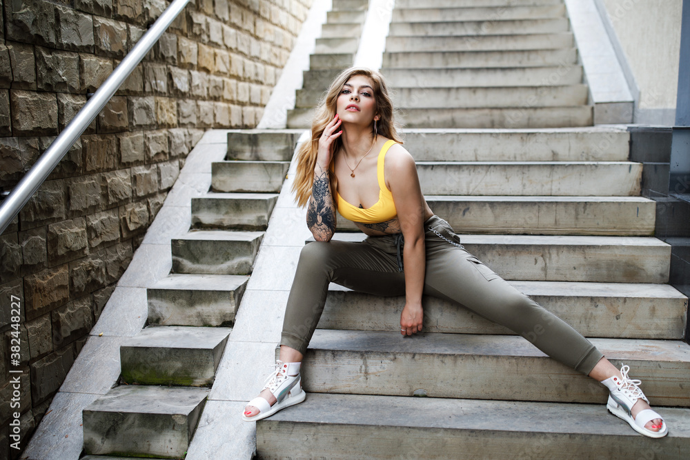 Street fashion summer portrait of beautiful woman sitting on stairs