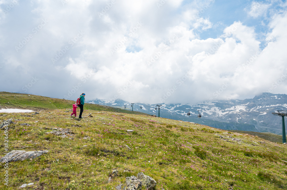 Mother and daughter hiking green alpine pastures.