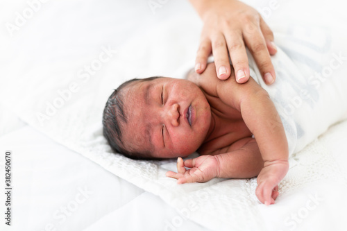 African American newborn baby or infant lying on white bed while mother nursing on her baby