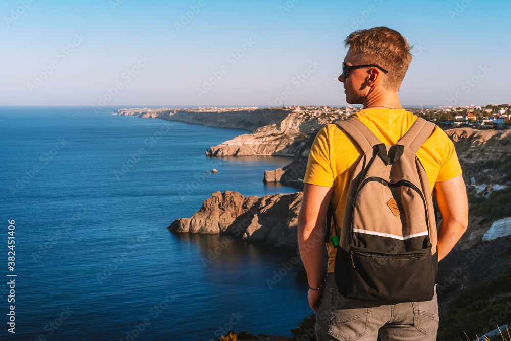 Fototapeta premium Young man with blond hair on vacation on the edge of the cliff of Cape Fiolent in Crimea, beautiful view of the Black sea