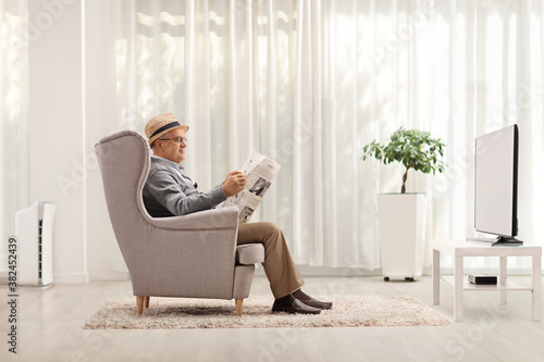 Mature man sitting in an armchair and reading a newspaper in a living room