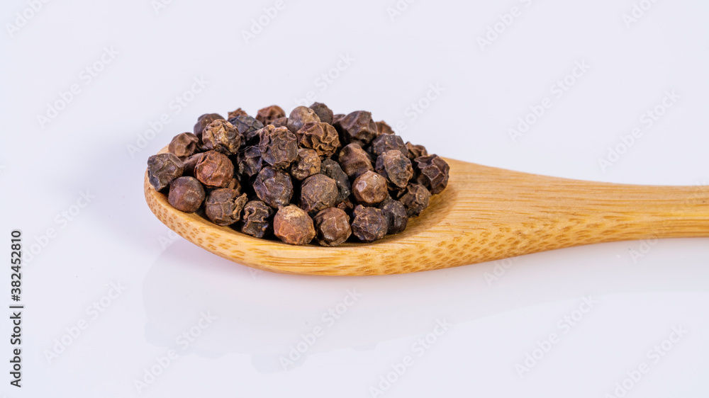 Obraz premium Black pepper corns on bamboo spoon isolated on white background