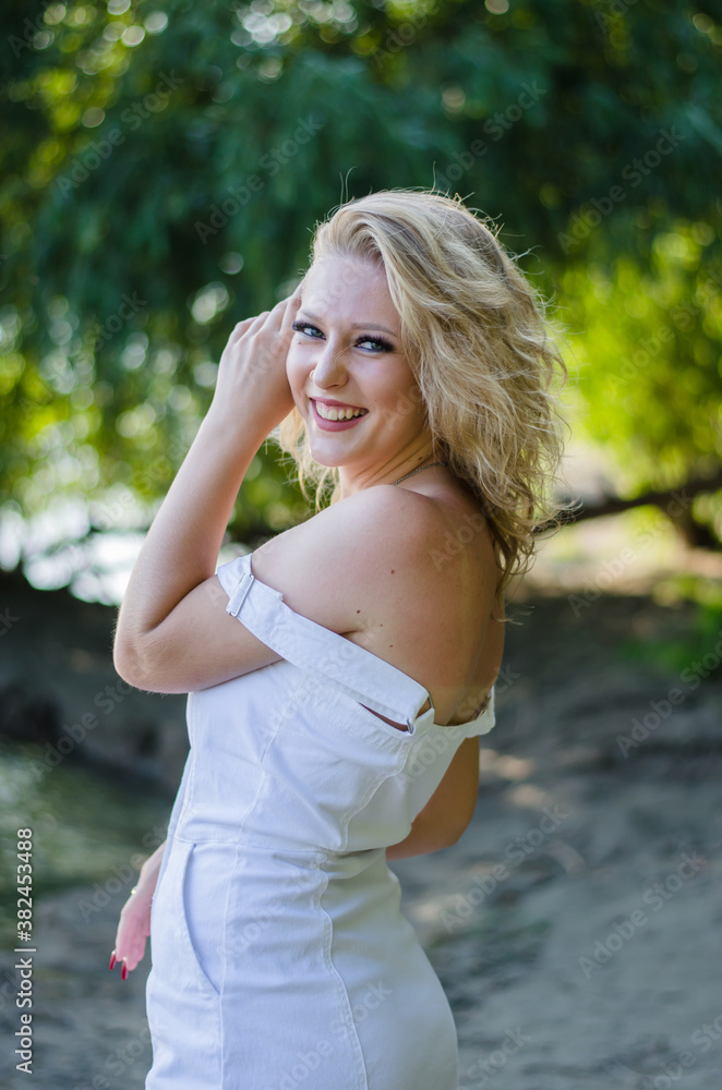 Beautiful girl looking at the camera and smiling. Blonde in white dress in nature Beautiful girl looking at the camera and smiling. Blonde in white dress in nature