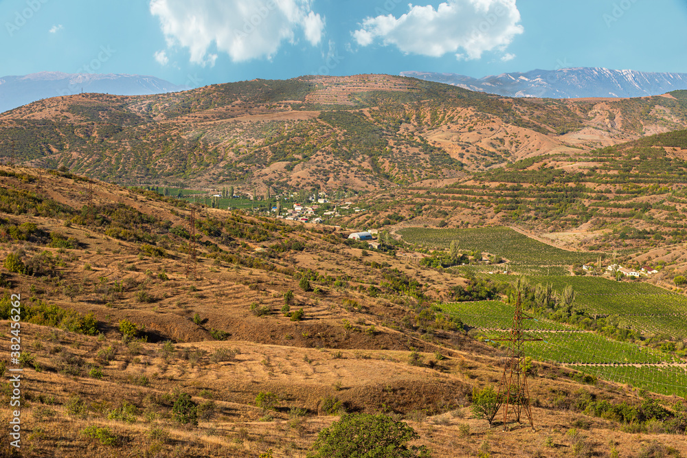 Landscape of the Crimean mountains, on a bright Sunny day, a gorge between the mountains with vineyards and a village located in the lowlands