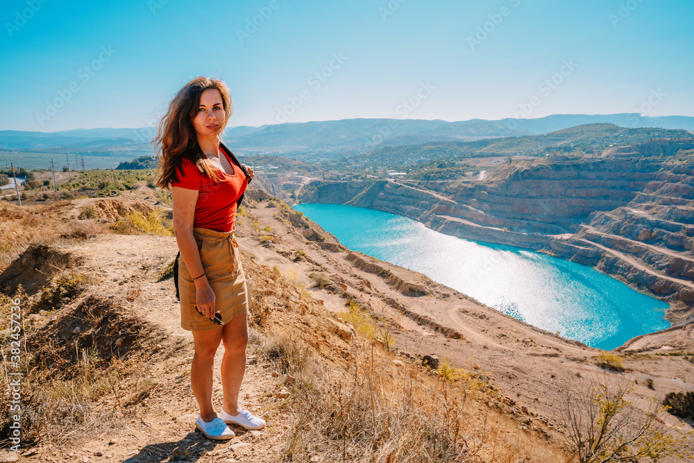 A beautiful woman in red clothes stands over a quarry with an azure lake, Kadykovsky quarry is a tourist natural attraction