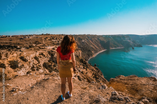 Rear view of traveler woman standing on cliff edge in front of amazing seascape. Freedom, travel and vacation concept.