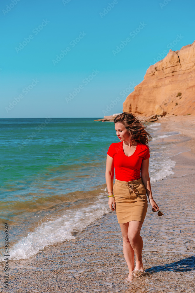 Charming brunette woman walks along the beach and admires the azure clear sea water, relaxing on the Black sea