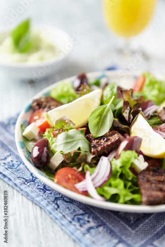 Tasty Salad with Grilled Beef Pieces, Cherry Tomatoes, feta Cheese and Kalamata Olives. Bright wooden background. Close up. 