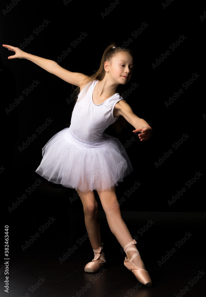 Naklejka premium Cute little girl in a tutu and pointe shoes is dancing in the studio on a black background.