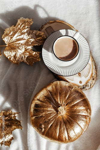 Autumn composition of shiny gold Pumpkin, maple leafes and cup of hot chocolate. Halloween decorations. trendy holiday concept. Golden autumn card.