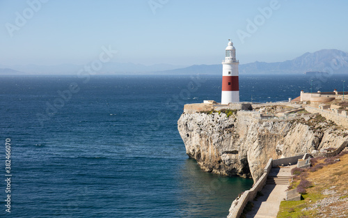 The red and white lighthouse of Gibraltar in sunshine in June. The Strait of Gibraltar and the mountains of the Spanish south coast can be seen in the background.