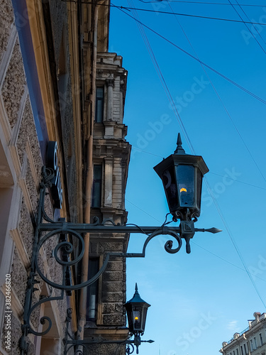 Old vintage black dark glass street lanterns hanging on textured wall of beautiful building in city of Saint Petersburg. Blue sky gradient. Ancient architecture