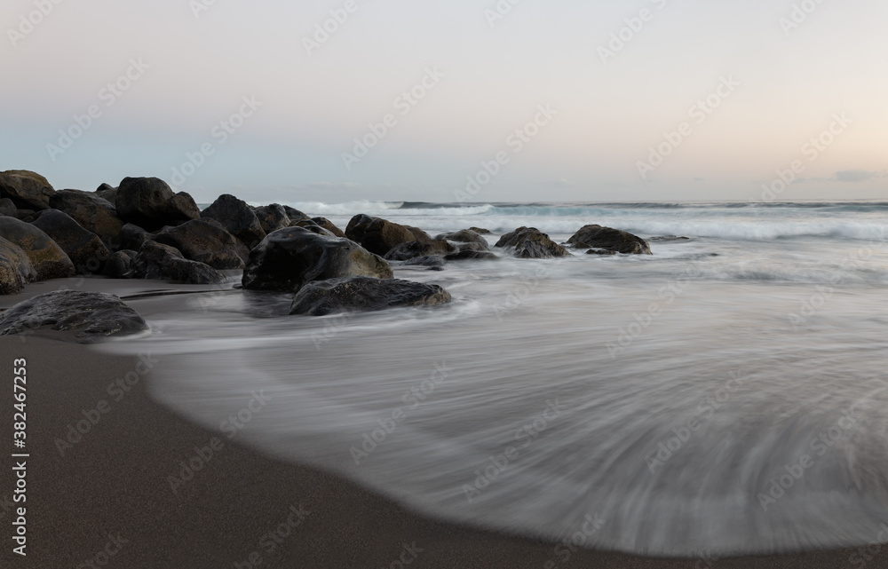 Soft waves on the beach. A long exposure of a sandy beach with stones and rocks on the Atlantic Ocean. It's early morning. The rocks shine just before sunrise.
