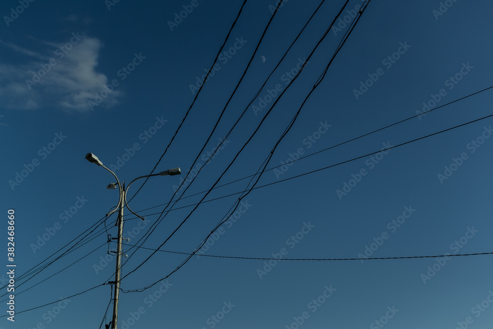 Ordinary city lamppost with three glass lamps. Black wires all around. Evening blue sky gradient background with white moon and cloud Ordinary city lamppost with three glass lamps. Black wires all around. Evening blue sky gradient background with white moon and cloud