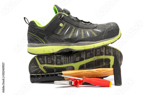Pair of black safety shoes with with green lining along with a hammer with wooden handle, a red pliers and a red Phillips screwdriver. With a white background.